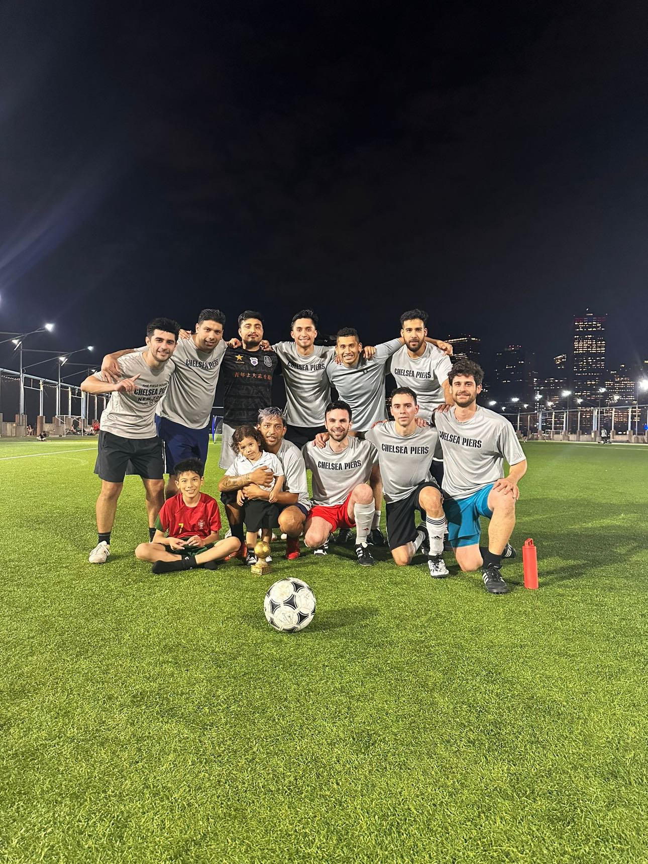Soccer team gathering after pickup game at night with city skyline in background